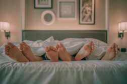 Photo of three pairs of feet sticking out from the blankets on a bed.